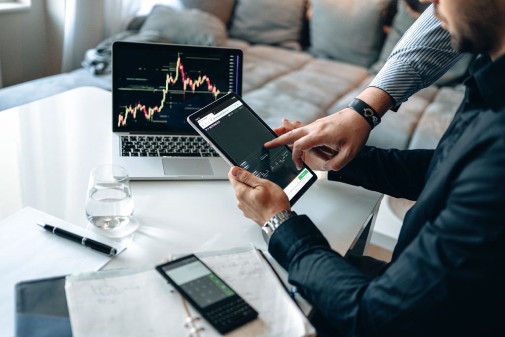 Professionals reviewing stock market trends on a tablet and laptop, discussing investment strategies.
