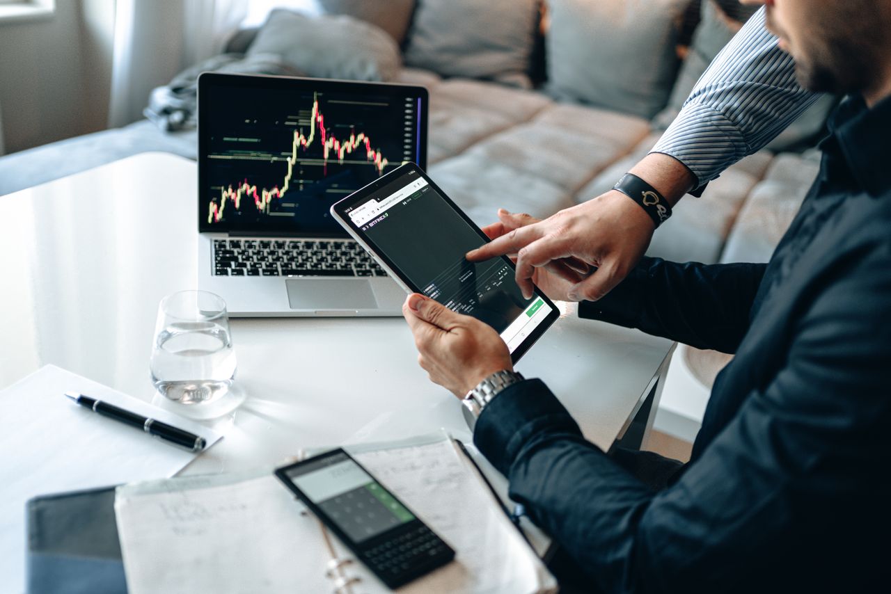 Professionals reviewing stock market trends on a tablet and laptop, discussing investment strategies.